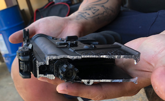 A man holding the remains of a rifle that has been cut up and destroyed.